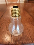 Light Bulb Shaped Clear Glass Jar With Gold Tone Screw Top 4.25" Tall. Fixed Price $9.00.